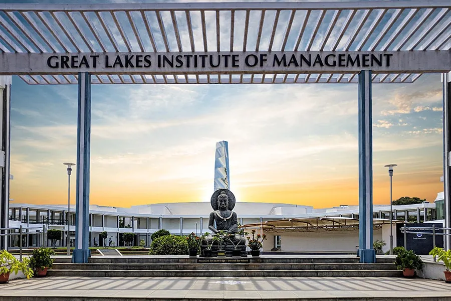 The entrance gateway of Great Lakes Institute of Management, with the campus buildings and the Buddha statue behind it at sunset
