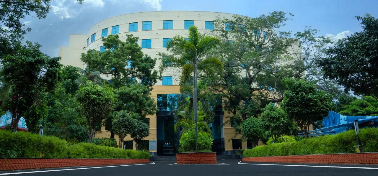A curved multi-storey campus building seen from the approach road, behind a line of trees