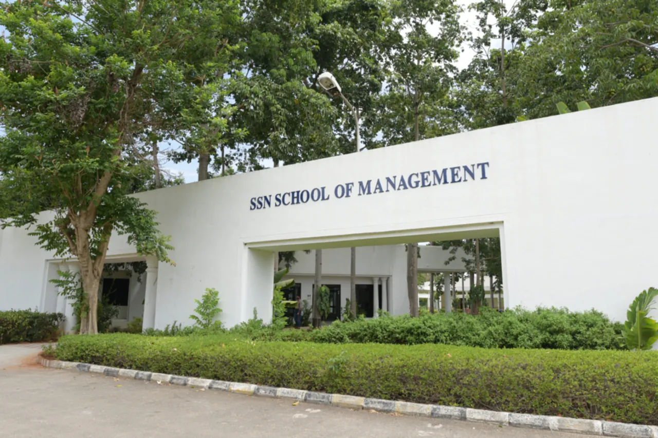 The white entrance wall of the SSN School of Management building, with its name on it, behind a hedge and trees