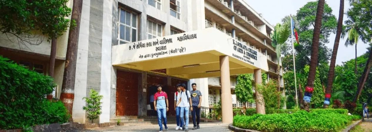 The entrance porch of K. J. Somaiya College of Arts and Commerce with its name board, three students walking out, garden to the right. Wide banner crop (1264 x 450).