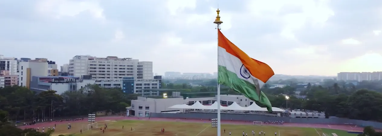 Wide view over the Somaiya Vidyavihar campus: the sports ground, the national flag on its mast and campus buildings behind. It is the home-page video poster on the engineering school's site, served from the parent university's domain somaiya.edu, and is the SAME image recorded for somaiya-vidyavihar-university.