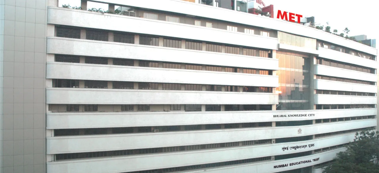 The MET Mumbai building (Bhujbal Knowledge City) seen from below, the MET sign on the roof and the trust's name on the facade.