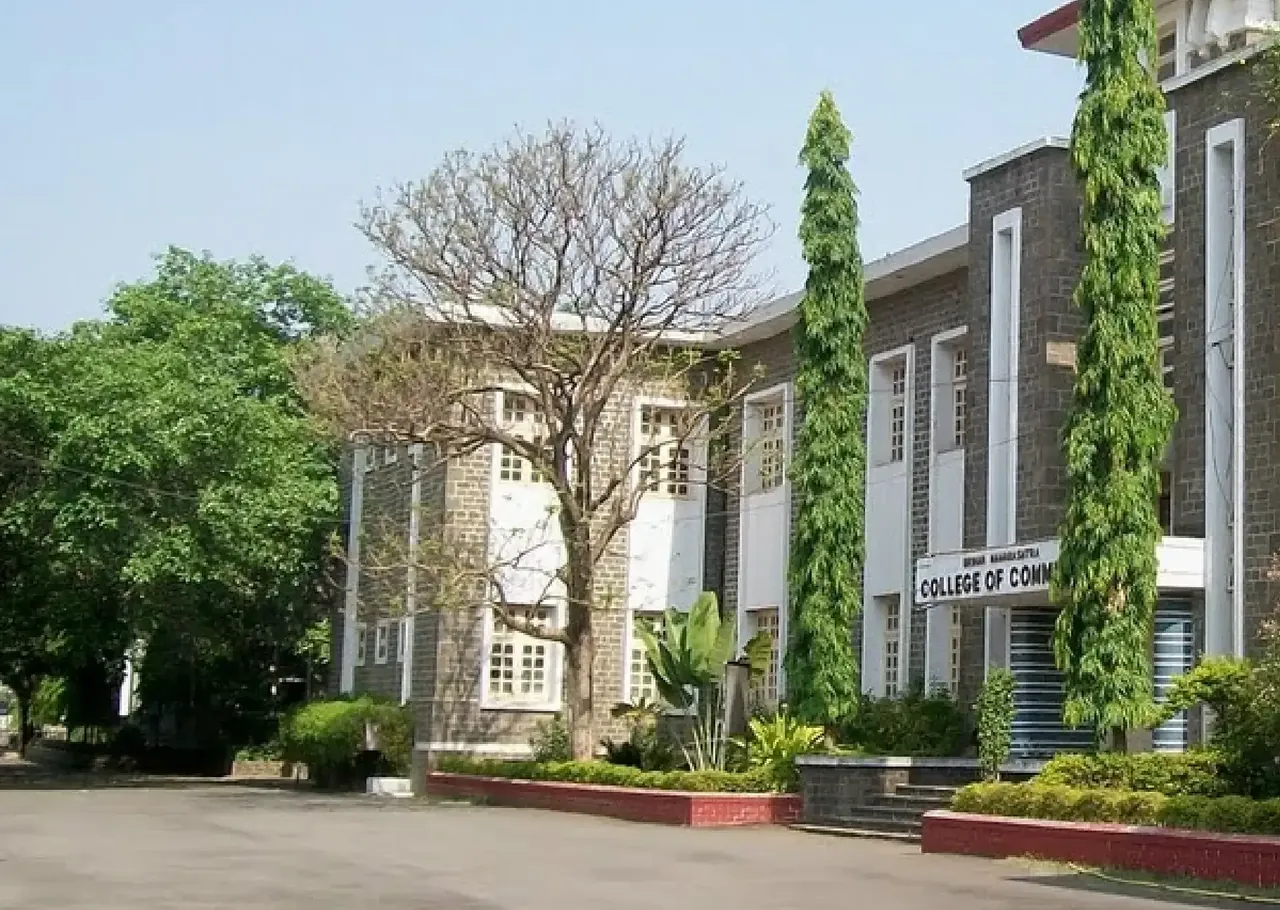 The stone main building of Brihan Maharashtra College of Commerce seen across the forecourt, with the college name board